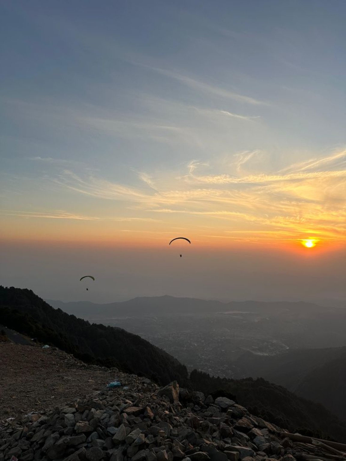 Paragliders silhouetted against a golden sunset over the hills